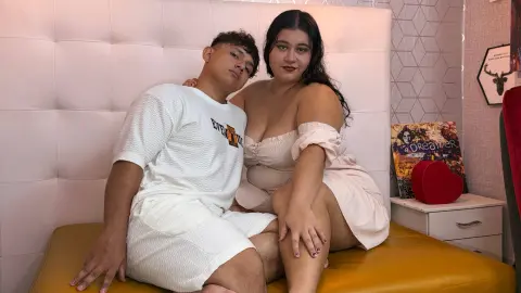 Young couple in white loungewear cuddling on a bed in a cozy, modern bedroom setting.