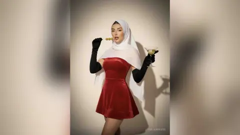 Elegant woman in a red velvet dress and white hijab eating olives in a sophisticated studio setting.