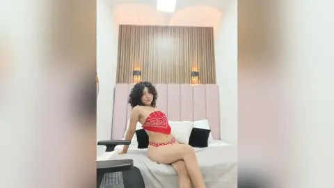 AkiraHayami poses on a white bed wearing a red patterned bandeau top and matching red undies.