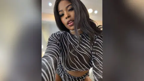 Glamorous woman in a sparkly black and silver striped long-sleeve top posing with a confident expression.