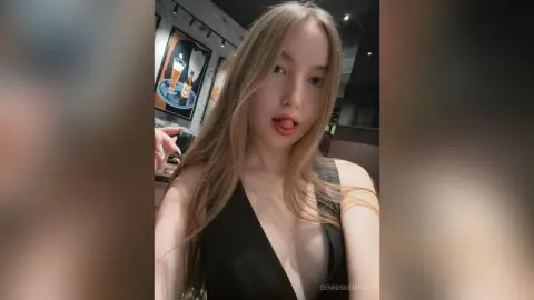 Blonde woman in a black halter top posing in a moody, dimly lit restaurant setting.