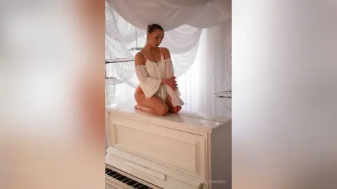 Elegant woman in a white flowing dress kneeling on a white piano in a dreamy, ethereal room.