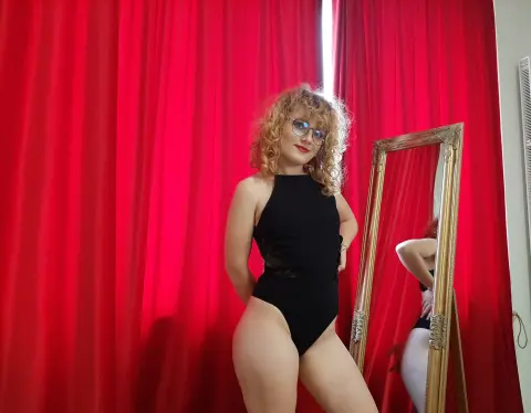 Curvy woman in a black bodysuit posing against red curtains in a glamorous indoor setting.