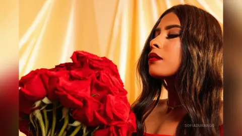 Beautiful woman with long wavy hair holding a large bouquet of red roses against a warm golden backdrop.