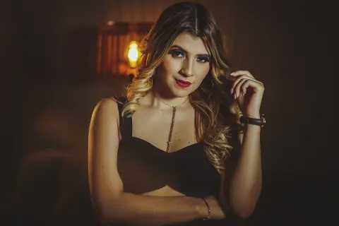 Elegant woman in a black tank top and gold necklace posing in warm, moody indoor lighting.