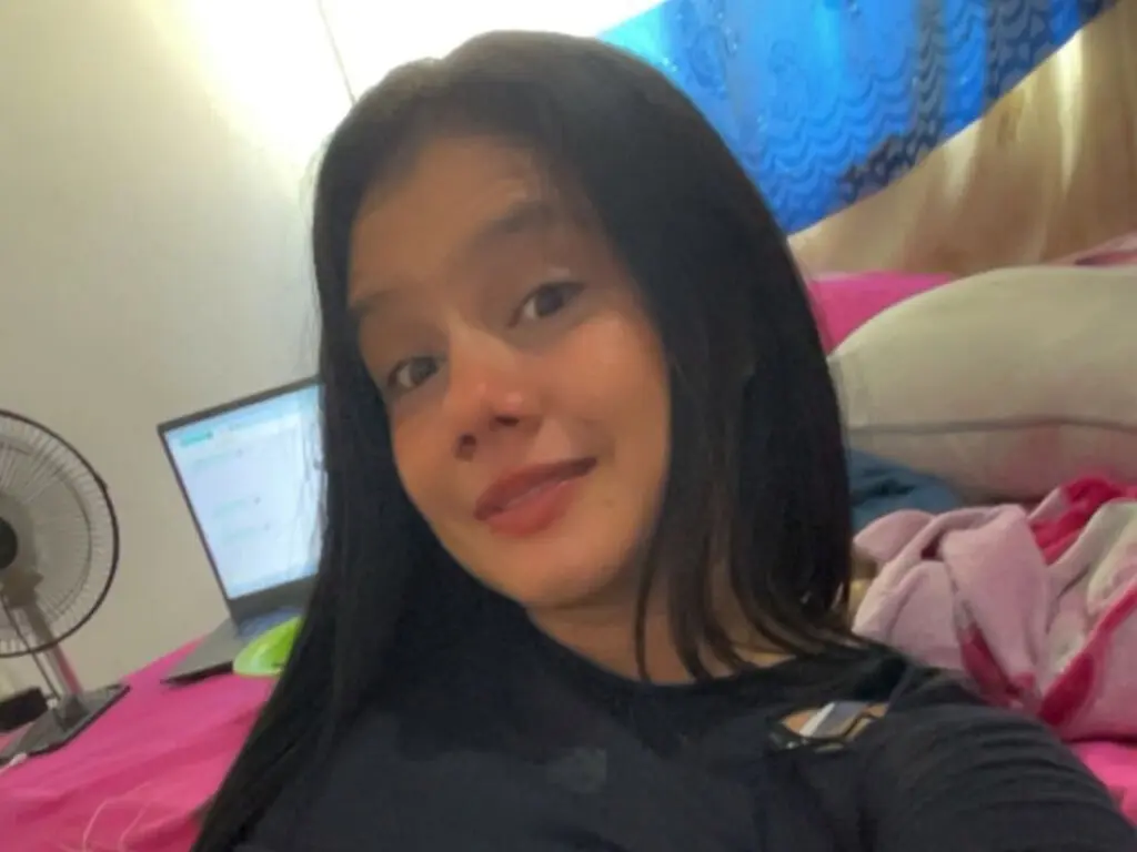 Smiling young woman in a black t-shirt relaxing in a cozy bedroom setting.