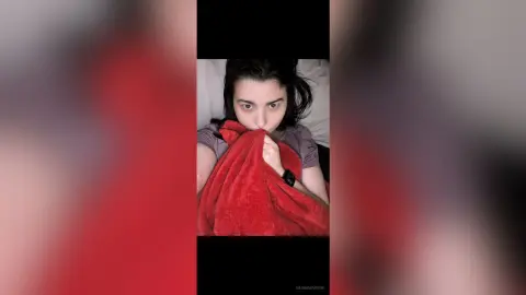 Young woman wrapped in a cozy red blanket sitting on a bed with a relaxed, peaceful mood.