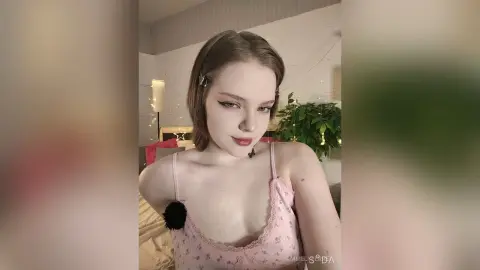 Young woman in a pink floral camisole posing in a cozy bedroom with warm lighting.