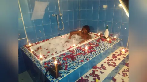 Relaxed woman relaxing in a bubble bath surrounded by glowing candles in a blue tiled bathroom.