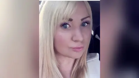 KarolinaBright looks directly at the camera with her long blonde hair and blue eyes, wearing a white top.
