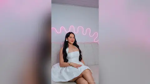 Young woman in a white cocktail dress sitting in a modern room with pink neon light decor.