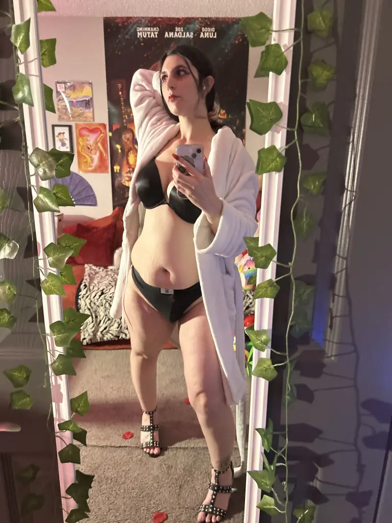 BonnieBlast looks directly at the camera with dark hair and dark lipstick, wearing a light pink camisole strap visible on her shoulder.