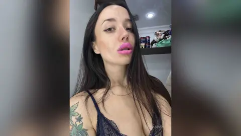 Young woman with long dark hair and pink lipstick wearing a navy lace camisole in a bright indoor setting.