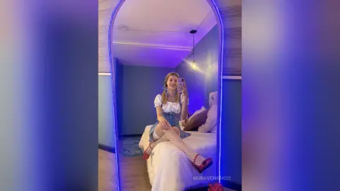Young woman in a white puff-sleeve top and blue skirt taking a selfie in a neon-lit bedroom mirror.