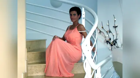 Elegant woman in a peach flowing gown sitting on marble stairs in a bright, modern interior.