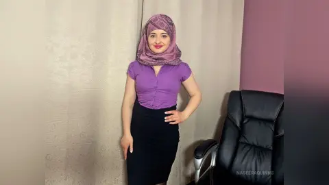 Smiling woman in a purple blouse and black skirt wearing a mauve hijab in a bright indoor setting.