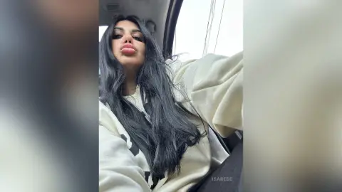 Young woman with long dark hair wearing a white sweatshirt sitting in a car with a relaxed mood.