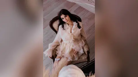 Elegant woman in a flowing white ruffled dress sitting on a vintage chair in a bright, dreamy room.