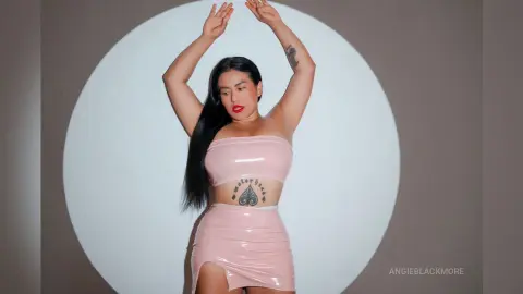 Glamorous woman in a pink latex two-piece outfit posing confidently against a white circular studio backdrop.