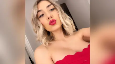 Blonde woman in a red strapless top making a playful pouty face in a bright indoor setting.