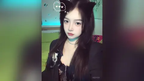 HedyIvy wearing cat ears and a black outfit with a silver necklace, looking at the camera in a bedroom setting.