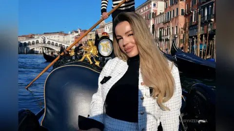 Blonde woman in a white tweed jacket enjoying a sunny gondola ride on a Venetian canal near Rialto Bridge.