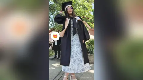 Happy female graduate in black cap and gown and floral dress celebrating outdoors on graduation day.