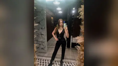 Stylish woman in a black jumpsuit posing in a modern, moody restaurant setting.