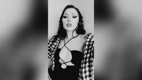 Moody black and white portrait of a woman in a black bodysuit and plaid shirt wearing headphones.