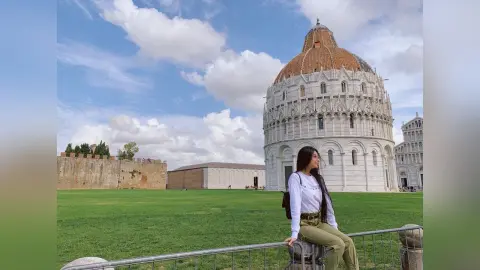 LucyMartin sits on a metal railing against a backdrop of a large white domed cathedral and a green lawn under a blue sky.