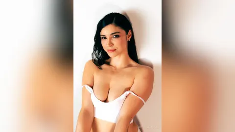 BrendaaLocke — BrendaaLocke poses against a white wall wearing a white strapless bra top.