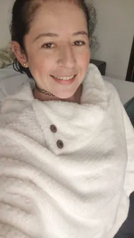 Smiling woman wrapped in a cozy white fleece blanket in a comfortable indoor setting.