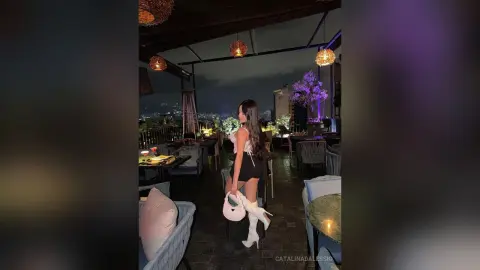 Stylish woman in a white top and black shorts standing on a luxury rooftop terrace at night.