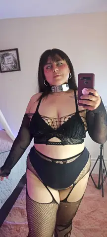 LuluPup poses in a black lace bra and high-waisted black bottoms with fishnet stockings and a silver collar.