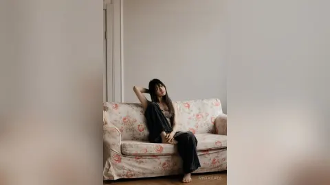 MintaTukes — MintaTukes sits on a floral patterned sofa wearing a black tank top and black pants.