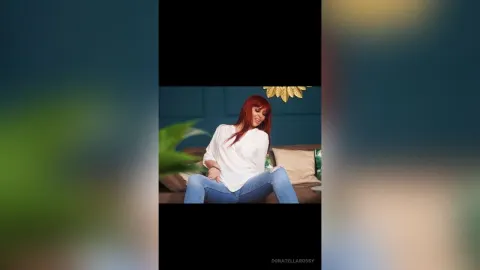 DonatellaRossy — DonatellaRossy sits on a brown sofa wearing a white shirt and blue jeans.