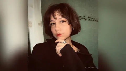 Young woman with short brown hair wearing a black jacket in a moody indoor setting.