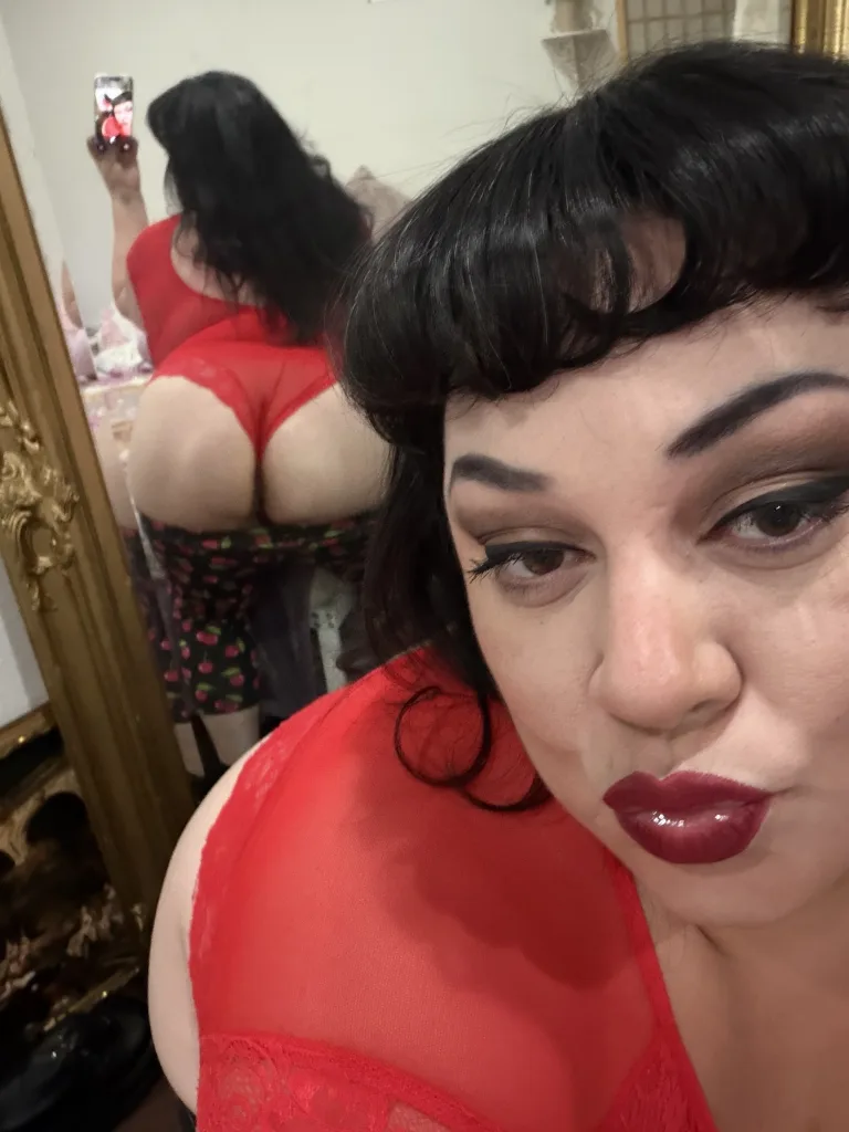 MistressJuliaJuggs poses in a black top that shows off her cleavage, looking directly at the camera with her dark hair down.