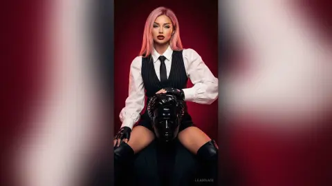 Pink-haired woman in a white shirt and black vest holding a dramatic black mask against a red background.