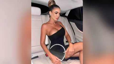 Glamorous woman in a sleek black dress sitting in a luxury car interior with a chic, confident mood.