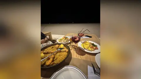 LucyMartin presents a large pan of paella served with lemon wedges and a glass of red wine on a wooden table.