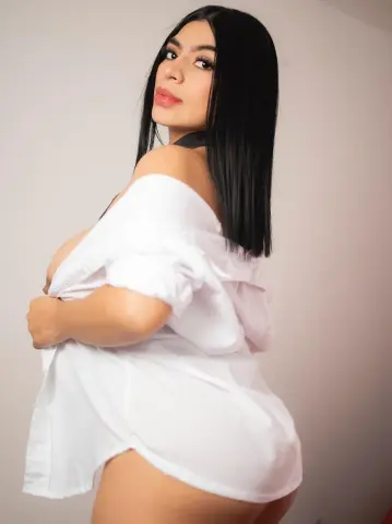 Young woman with long black hair wearing an oversized white shirt in a bright, minimalist indoor setting.