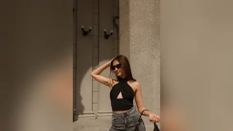 Stylish woman in a black halter top and denim jeans posing outdoors in warm sunlight.