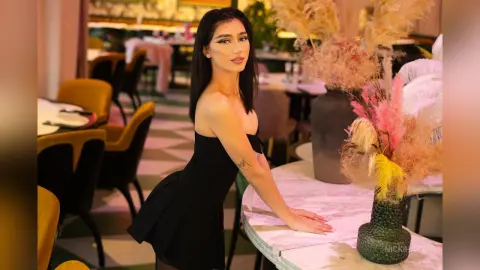 Elegant woman in a black strapless dress posing at a luxury restaurant with floral decor.