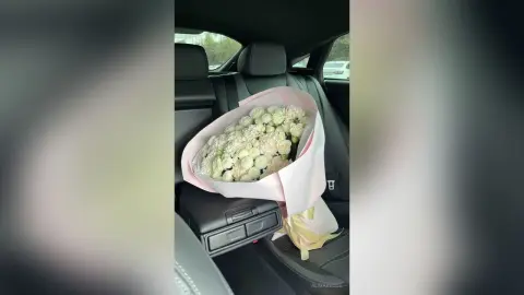 Large bouquet of fresh white flowers in pink wrapping sitting on a black leather car seat.