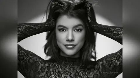 Portrait of a beautiful woman in a black lace top posing with hands in hair in a moody black and white studio setting.
