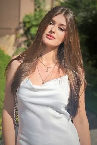 Young woman in a white satin camisole top posing outdoors in soft sunlight.