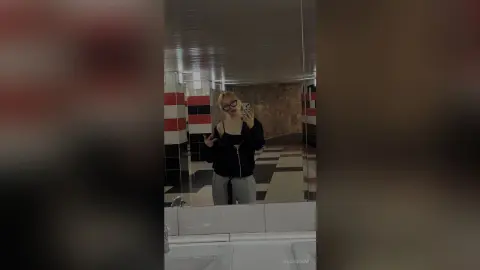EloiseGow takes a mirror selfie in a bathroom, wearing a black zip-up hoodie and grey sweatpants.