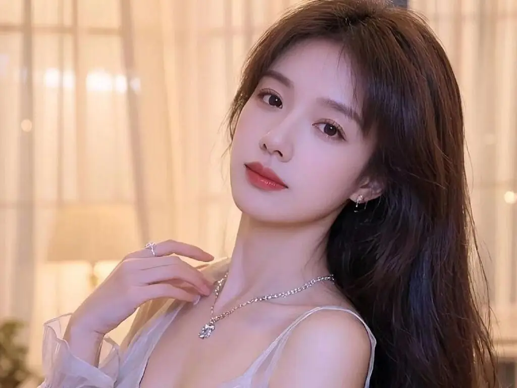 Elegant young woman in a white lace dress and silver necklace posing in a soft, warm indoor setting.