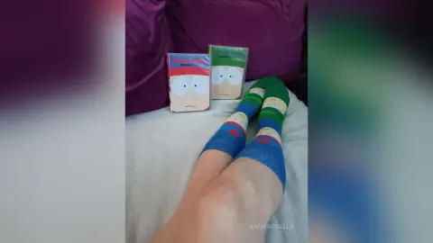 Person wearing South Park character socks relaxing on a white bed with themed pillows.